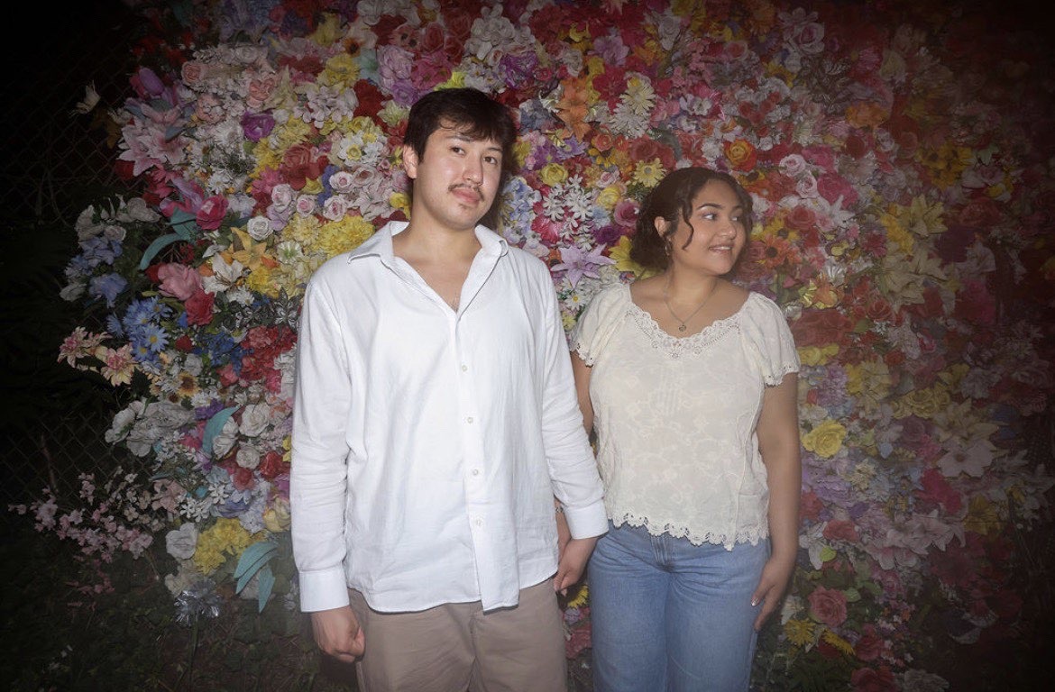 Eli and Ethan holding hands in front of a wall of flowers at night