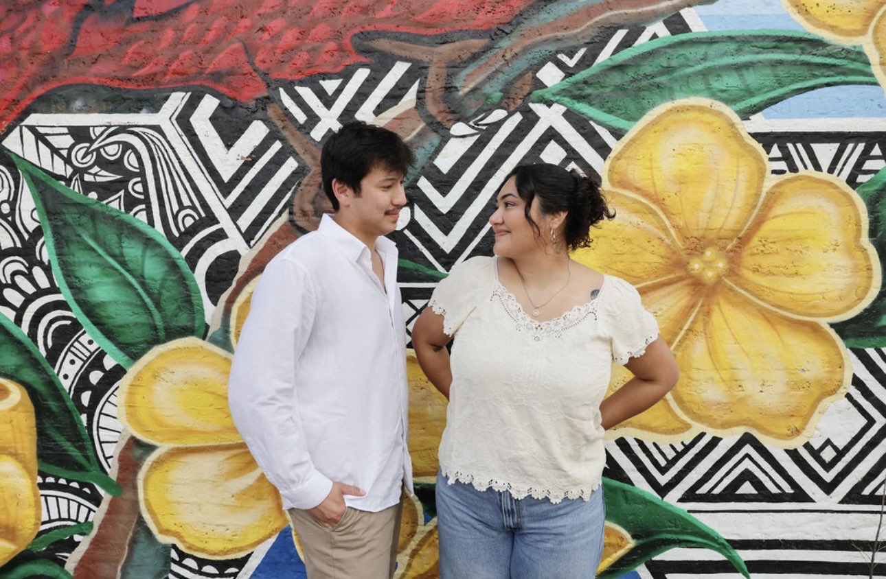 Eli and Ethan smiling at each other in front of a mural with big yellow flowers